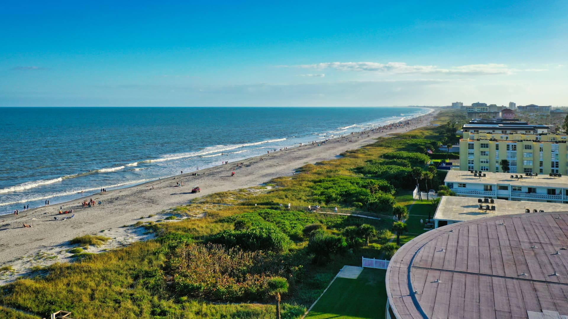 Aerial photograph looking down on the Brevard County coastline, with pale sand beach meeting turquoise ocean water and gentle waves, representing the beachside communities we serve.